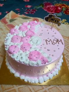 a birthday cake with pink and white flowers on it that says mom in gold lettering