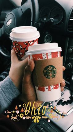 two people holding up coffee cups in their hands while sitting in the drivers seat of a car