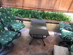 some chairs and a table are sitting on the outside patio with plants in the background