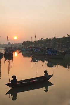 two people in a small boat on the water at sunset or dawn, with boats and palm trees in the background