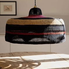 a woven lamp shade hanging from a wooden table in a room with pictures on the wall