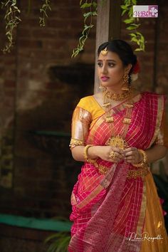 a woman in a red and yellow sari standing under a tree with her hands on her hips