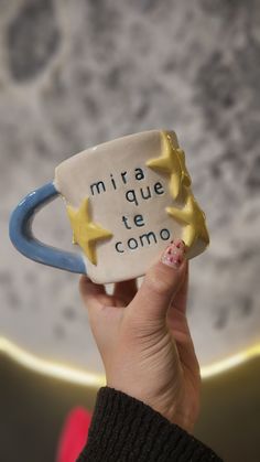 a hand holding up a ceramic mug with stars on it and the words mira que te como