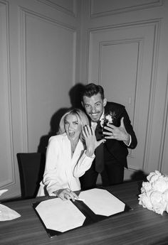 a man and woman sitting at a table with papers in front of them, posing for the camera