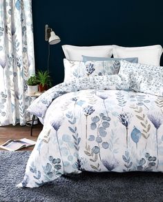 a bed with blue and white comforters in a bedroom next to a window filled with curtains