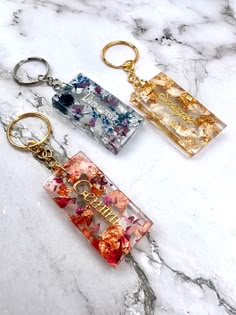 two key chains with flowers on them sitting on a marble surface