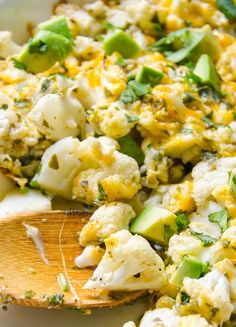 a wooden spoon filled with food on top of a white plate next to broccoli and cauliflower