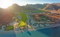 an aerial view of a golf course in the desert with mountains and water behind it