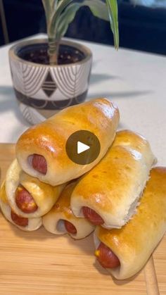 three hot dogs wrapped in bread on top of a cutting board next to a potted plant