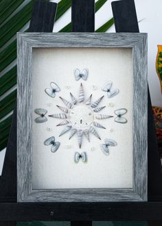 an image of a framed artwork with seashells and shells in the center on a black stand