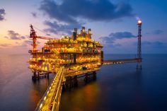 an oil and gas platform in the middle of the ocean at night with lights on