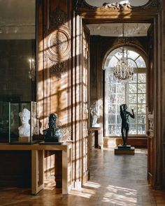 the sun shines through an arched window into a room with sculptures and chandeliers