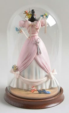 a figurine is under a glass dome on a wooden base with an image of a woman in a pink dress