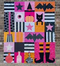 a colorful quilt hanging on the side of a brick wall next to a black cat