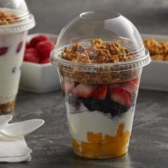 a plastic cup filled with yogurt, granola and strawberries on top of a table