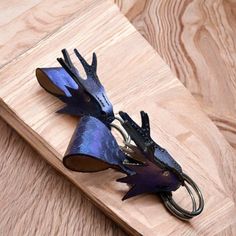 two metal birds on a wooden board with strings attached to it's ends, one is purple and the other is black