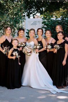 a group of women standing next to each other wearing black dresses and holding bouquets