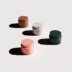 four different colored containers sitting on top of a white surface with shadows coming from them