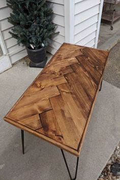 a wooden table sitting on top of a sidewalk next to a potted pine tree