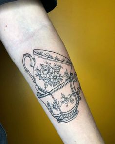 a tattoo on the arm of a woman with a tea cup and flowers in it