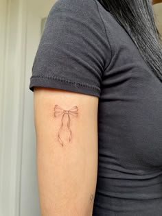 a woman's arm with a bow tattoo on the left side of her arm