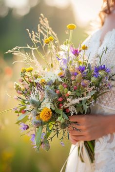 a bride holding a bouquet of wildflowers and other flowers in her hands, outdoors