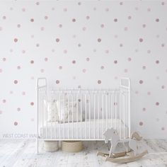 a white crib with pink polka dot wallpaper and rocking horse in the corner