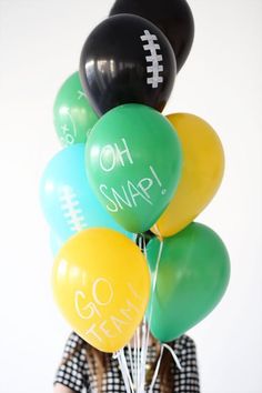 a woman holding balloons that say oh snap go team and have footballs on them