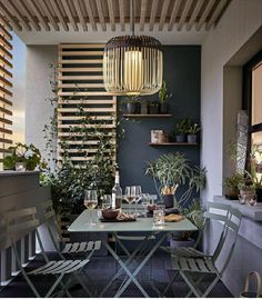 an outdoor dining area with green chairs and wooden slatted walls, potted plants on either side