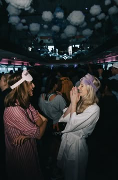 two women standing next to each other in front of a ceiling full of lights and balloons