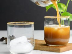 a person pouring orange juice into a glass with ice cubes next to it on a cutting board