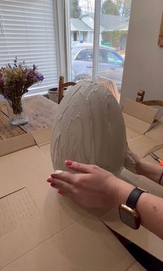 a woman is making a sculpture out of clay on a table in front of a window