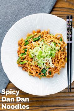 a white plate topped with noodles and veggies next to chopsticks on a wooden table