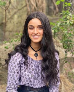 a woman with long black hair wearing a purple top