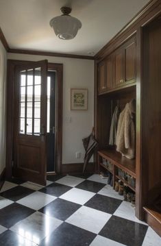 a hallway with black and white checkered floor, coat rack, and entry door