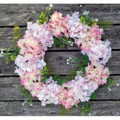 a wreath with pink and white flowers hanging on a wooden wall in front of a door