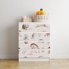 a white dresser topped with drawers covered in animal wallpaper next to a basket filled with pumpkins