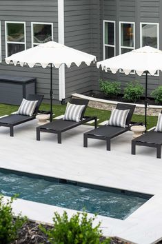 lounge chairs and umbrellas on the side of a house near an outdoor swimming pool