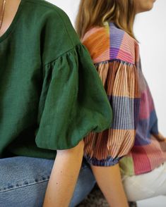 two women sitting on the ground, one wearing a green top and the other a multicolored blouse