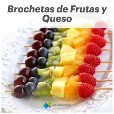 a white plate topped with fruit skewers on top of a wooden table next to a