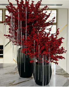 two black vases filled with red flowers on top of a marble counter next to each other