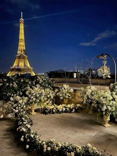 the eiffel tower lit up at night with white flowers in the foreground