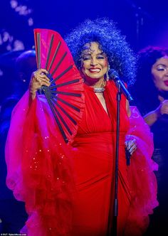 a woman in a red dress holding a fan and singing into a microphone on stage