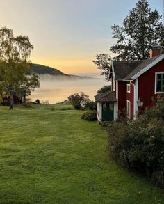 a red house sitting in the middle of a lush green field next to a body of water