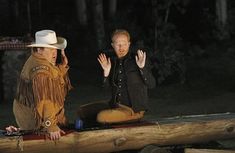 two men sitting on a log talking to each other