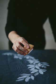 a woman is holding something in her hand while sitting at a table with a flower design on it