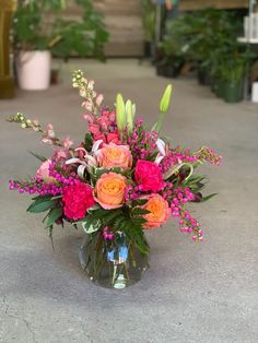 a vase filled with pink and orange flowers on top of a cement floor next to potted plants