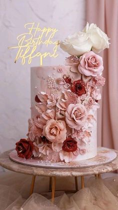 a white cake with pink and red flowers on it sitting on top of a table