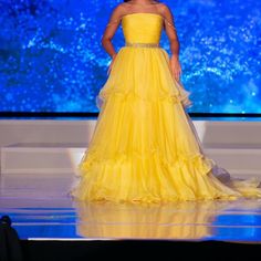 a woman in a yellow dress standing on a stage with her hands on her hips