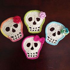 three crocheted skulls with flowers on them sitting on top of a wooden table